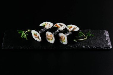 Siyah arka planda beyaz pirinç ve peynirli füme yılan balığı suşisi.
