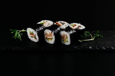 Siyah arka planda beyaz pirinç ve peynirli füme yılan balığı suşisi.