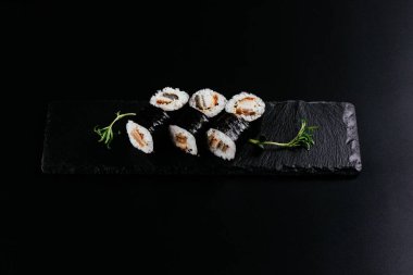 Siyah arka planda beyaz pirinç ve peynirli füme yılan balığı suşisi.