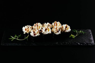 Siyah arkaplanda beyaz mayonez ile servis edilen suşi ruloları. 