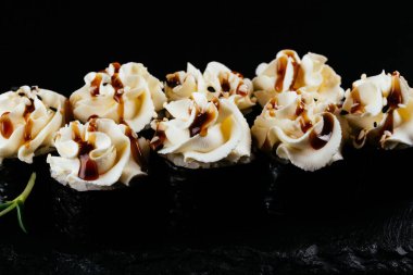 Siyah arkaplanda beyaz mayonez ile servis edilen suşi ruloları. 