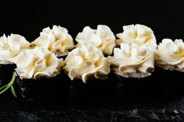 Siyah arkaplanda beyaz mayonez ile servis edilen suşi ruloları. 