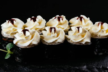 Siyah arkaplanda beyaz mayonez ile servis edilen suşi ruloları. 