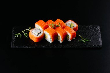 Siyah zemin üzerinde beyaz pirinç ve peynirli kırmızı somon suşi ruloları.