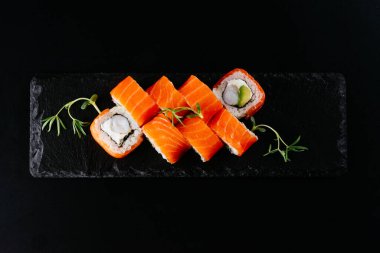 Siyah zemin üzerinde beyaz pirinç ve peynirli kırmızı somon suşi ruloları.