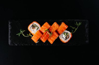 Siyah zemin üzerinde beyaz pirinç ve peynirli kırmızı somon suşi ruloları.