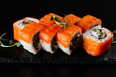 Siyah zemin üzerinde beyaz pirinç ve peynirli kırmızı somon suşi ruloları.