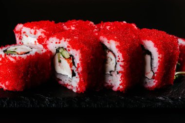 Kırmızı havyar suşi ruloları. Siyah arka planda beyaz pirinç ve peynir.
