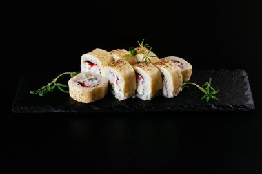 Siyah zemin üzerinde beyaz pirinç ve peynir ile beyaz balıklı suşi ruloları.