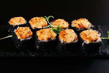 Somonlu suşi rulosu ve siyah arka planda susam.