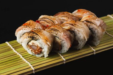 Siyah arka planda somon ve sebzeli suşi rulosu.