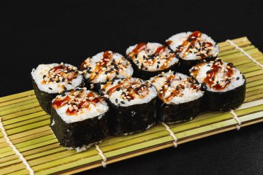 Siyah arka planda somon ve sebzeli suşi rulosu.