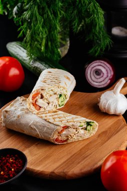 Ahşap bir arka planda sebzeli ve baharatlı ev yapımı tavuk dürümü. 