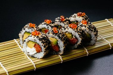 Somonlu suşi rulosu ve siyah arka planda avokado.