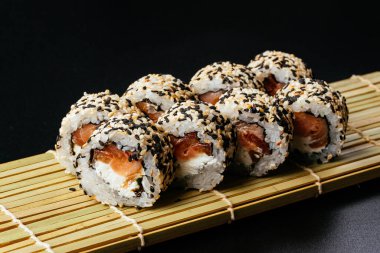 Somonlu suşi rulosu ve siyah arka planda avokado.