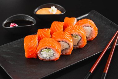 Siyah taş arka planda somonlu suşi rulosu. 