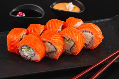 Siyah taş arka planda somonlu suşi rulosu. 