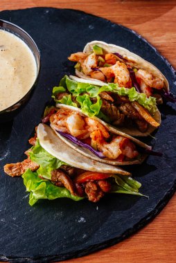 Tahta arka planda tavuk, sebze ve soslu Meksika tacoları..