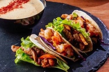 Tahta arka planda tavuk, sebze ve soslu Meksika tacoları..