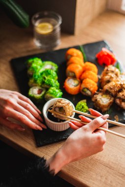 woman eating sushi with soy sauce on wooden table