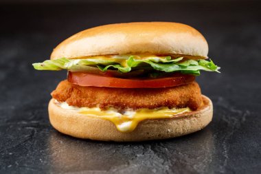 Siyah arka planda tavuk ve marullu yakın plan burger.
