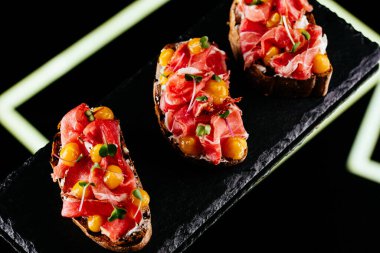 Siyah arka planda salam, peynir ve sebzeli bruschetta.