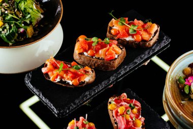 Siyah arka planda somon, avokado, domates ve peynirli bruschetta.