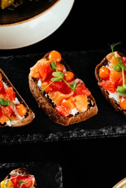 Siyah arka planda somon, domates ve fesleğenli bruschetta.