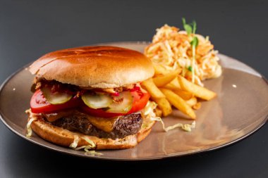 Sığır etli, peynirli ve domatesli hamburger, marul ve soğanlı patates kızartması, ketçap ve sos.