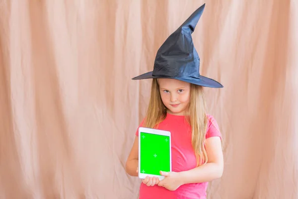 Retrato de una chica en un sombrero de bruja con una maqueta verde pantalla de la tableta espacio de copia de Halloween —  Fotos de Stock