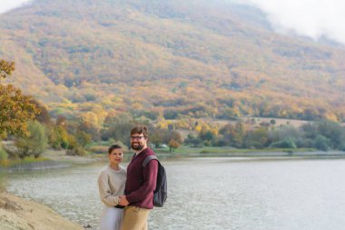 Sonbaharda göl kenarındaki ormanda sıcak örülü kazaklarla tatilde olan aile çifti.