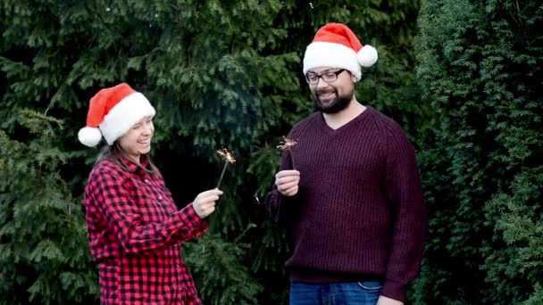 Šťastný milující pár v lásce stojí na pobřeží v blízkosti vánočních stromků a drží jiskry — Stock video