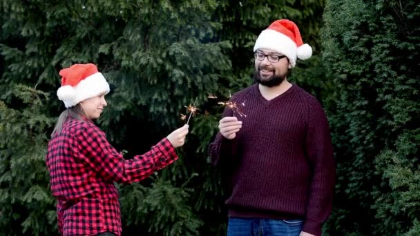 Міжнародна пара святкує Різдво і Новий рік на відкритому повітрі в капелюхах Санта Клауса, тримаючи блискавки — стокове відео