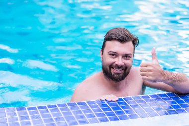 Positive handsome smiling man in swimming pool in summer scenery a thumbs up outdoors