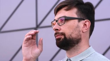 Genç, yorgun, sakallı, stil sahibi adam yavaş çekimde gözlüğünü çıkarıyor.