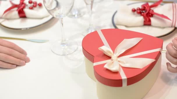Close-up de mãos femininas abrir uma caixa de presente em forma de coração em uma data em um restaurante dos namorados — Vídeo de Stock