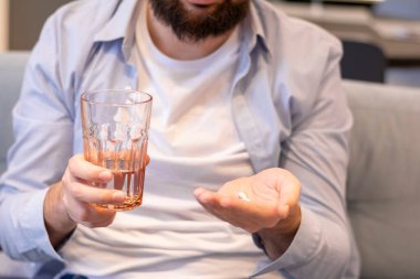 Sabahları elinde bir bardak su, elinde haplar ve vitaminler olan bir adam.