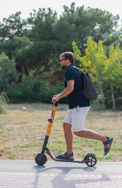 Stylish young man rides a scooter to work in the park — Stock Photo, Image