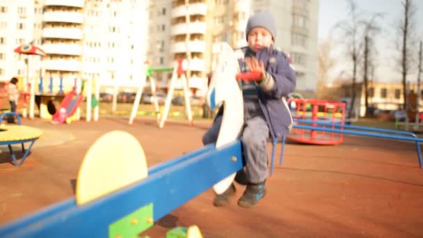 Cheerful boy in a blue dress on a swing. — Stock Video