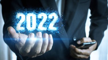 İş adamı, siyah arka planda parlayan ışıkla 2022 numaralı yeni yılın sanal görüntüsünü elinde tutuyor. Hedef planlama, yeni bir çağın başlangıcı. Pazarlama planları ve iş büyümesi