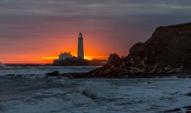 İngiltere 'nin kuzeydoğusundaki Whitley Körfezi' ndeki St. Mary Deniz Feneri 'nde muhteşem bir gün doğumu. Gökyüzü renk içinde patlıyor.