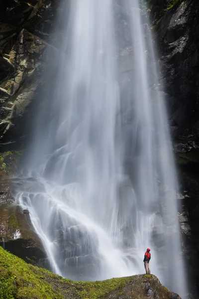 Giovane uomo in piedi vicino a una grande cascata Foto Stock