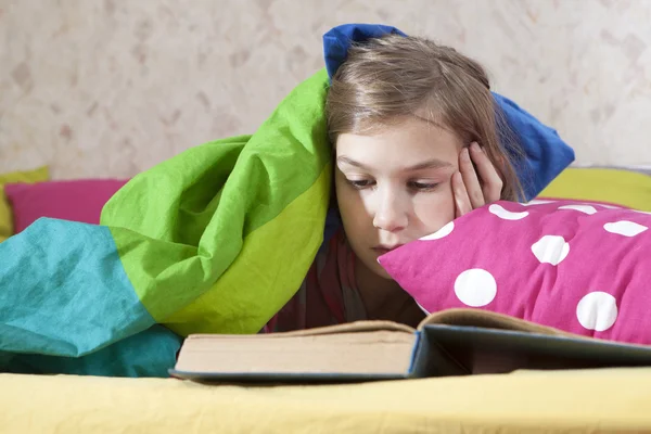 Flicka läsning i sängen under filt — Stockfoto