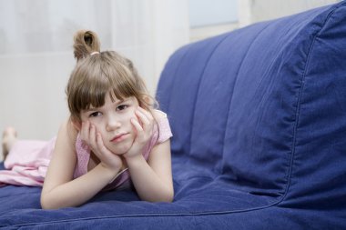 cute sceptical  little girl lying on sofa clipart