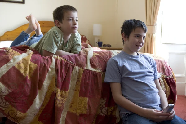 Menino com um controle remoto deitado em seu estômago e assistindo TV — Fotografia de Stock