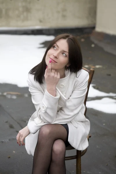 Portrait young woman in white overcoat sitting on chair — Stock Photo, Image