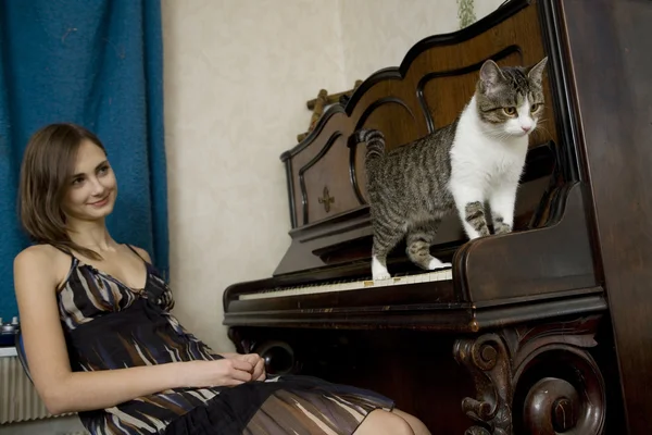 young woman is watching cat walking on piano