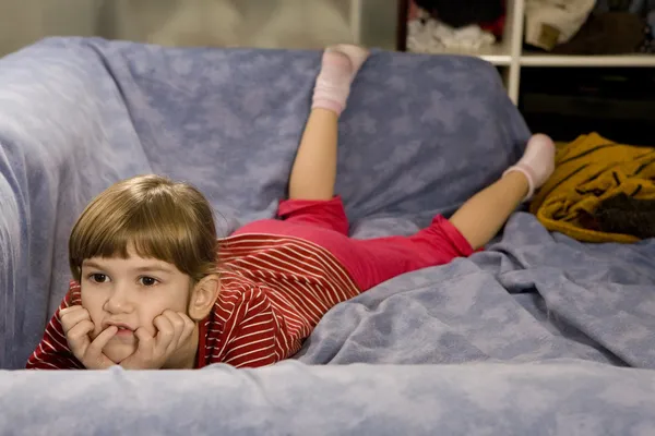 Kleines süßes Mädchen vor dem Fernseher auf dem Sofa liegend — Stockfoto