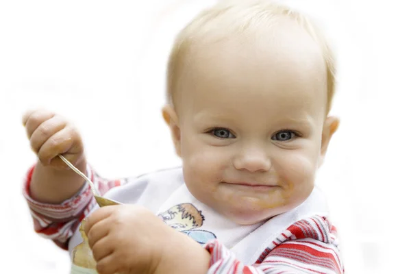 Bellissimo bambino dagli occhi azzurri che mangia salsa di mele con un cucchiaio isolato in bianco — Foto Stock