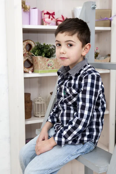 一个可爱的小男孩，坐在楼梯附近的五斗橱上的肖像 — 图库照片
